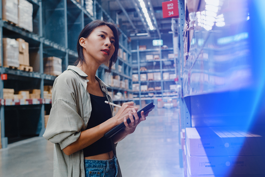 Woman in warehouse taking notes on tablet